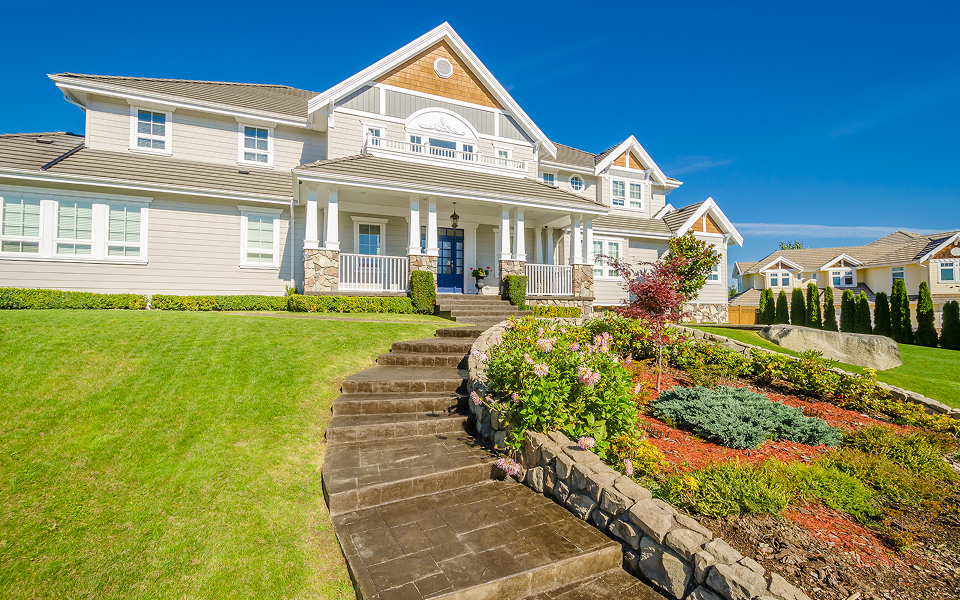 Two-story residence with a blue front door, stone walkway, and landscaped front garden under a clear sky.